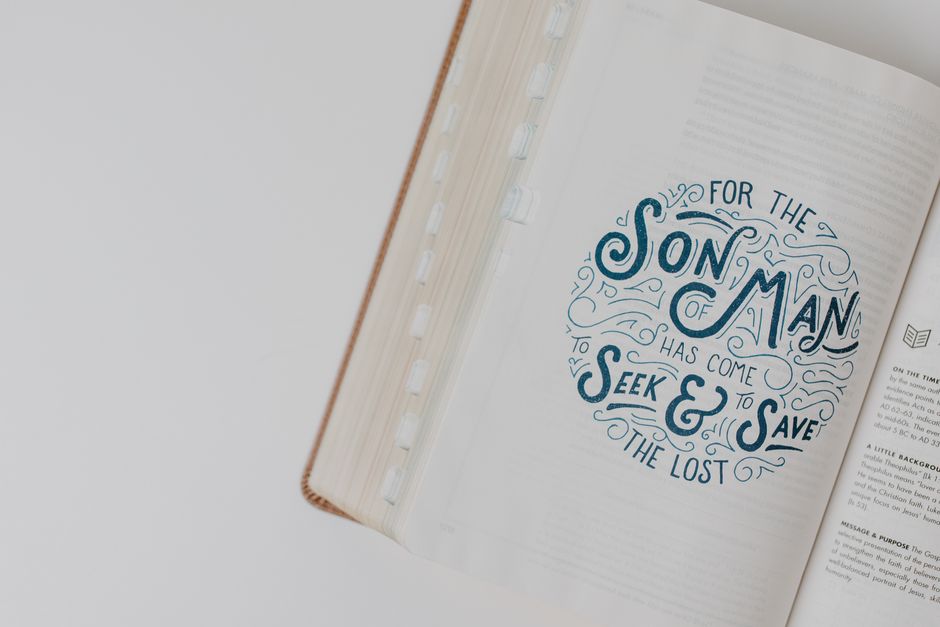 A close-up image of an open book with a decorative quote on the right page, which reads 'For the Son of Man has come to seek and save the lost' in blue and black lettering with ornate design elements.